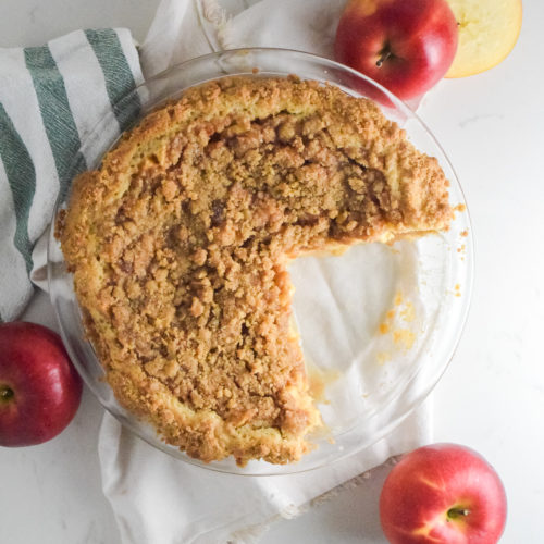 Apple Pie with crumble topping and cookie crust in a glass pie plate with red apples in background