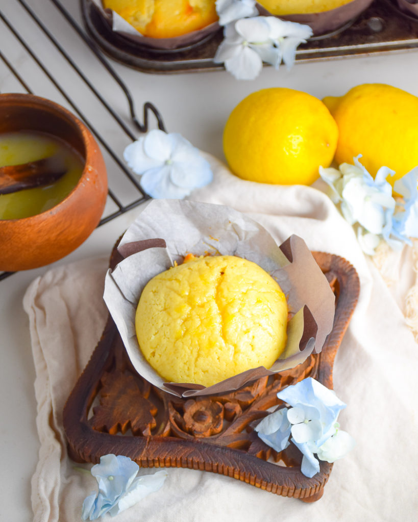 Yellow Lemon Cake in Muffin Paper on brown wooden trivet with cream colored napkin and blue flowers