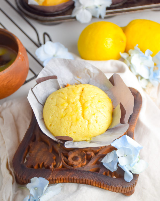 Yellow Lemon Cake in Muffin Paper on brown wooden trivet with cream colored napkin and blue flowers and lemons