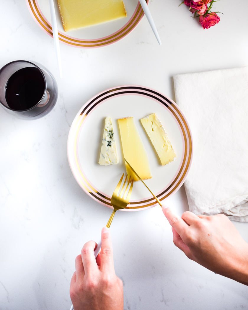 Woman's hands cutting cheese on a plate with a glass of red wine on the left