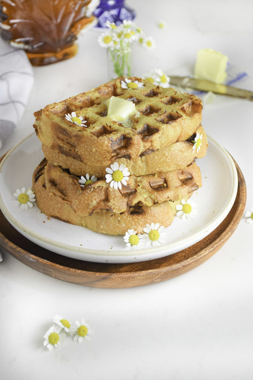 stack of french toast waffles on a white plate with pat of butter on top and chamomile flowers