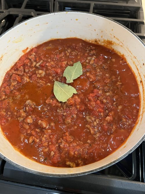 red sauce in a white pot on stove with two bay leaves on top