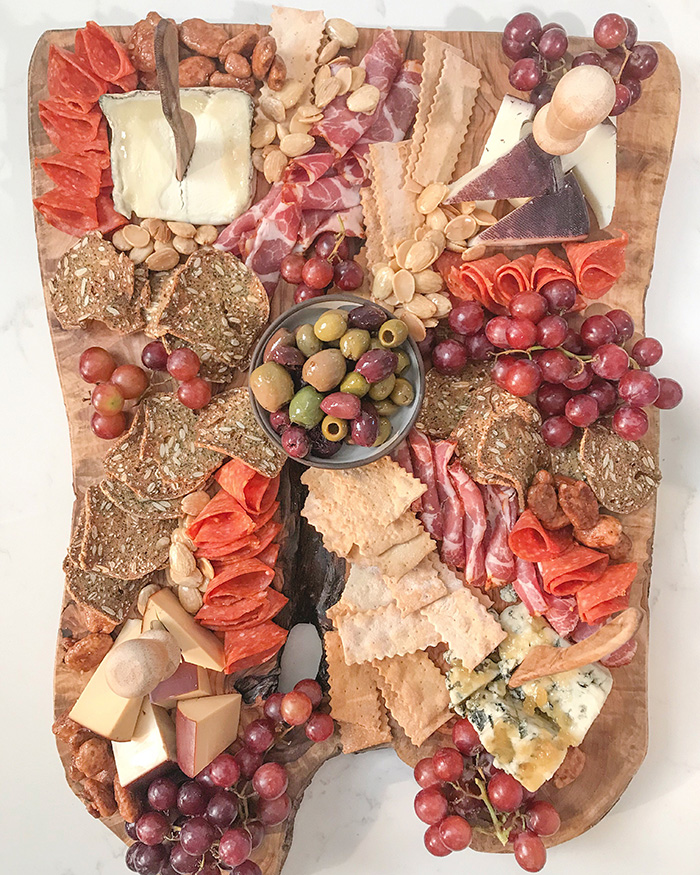Large olive wood board filled with cheeses, meats, olives and grapes and nuts